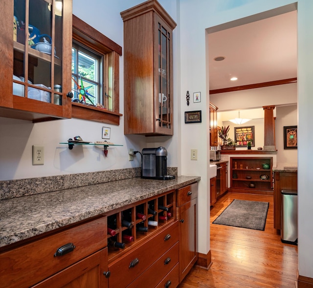 582 Summit Ave, Saint Paul, MN 55102 - kitchen featuring light wood-style flooring, glass insert cabinets, brown cabinets, ornate columns, and dark stone counters