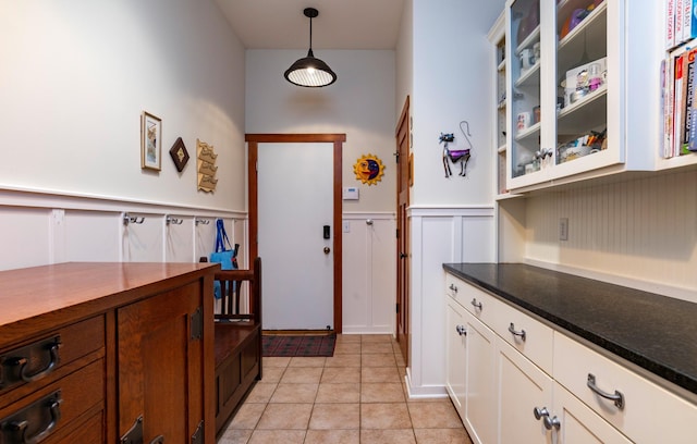 582 Summit Ave, Saint Paul, MN 55102 - kitchen with dark countertops, glass insert cabinets, a wainscoted wall, light tile patterned floors, and a decorative wall