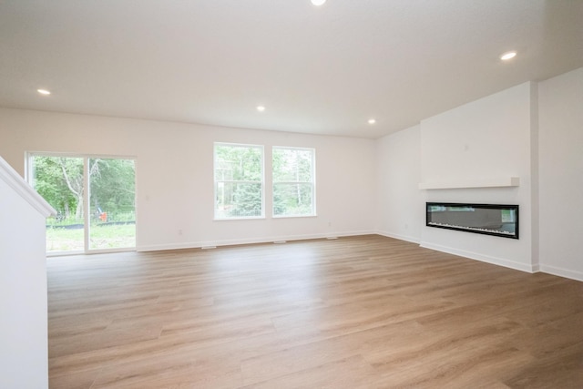 9706 Jasmine Ave NE, Hanover, MN 55341 - unfurnished living room featuring plenty of natural light, light wood-style floors, recessed lighting, and a glass covered fireplace
