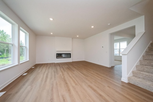 9706 Jasmine Ave NE, Hanover, MN 55341 - unfurnished living room featuring light wood finished floors, stairway, recessed lighting, and a glass covered fireplace