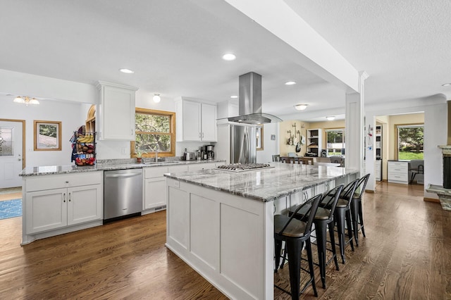 1281 Minnehaha Pkwy, Minneapolis, MN 55419 - kitchen with appliances with stainless steel finishes, island exhaust hood, white cabinets, a kitchen island, and a breakfast bar area