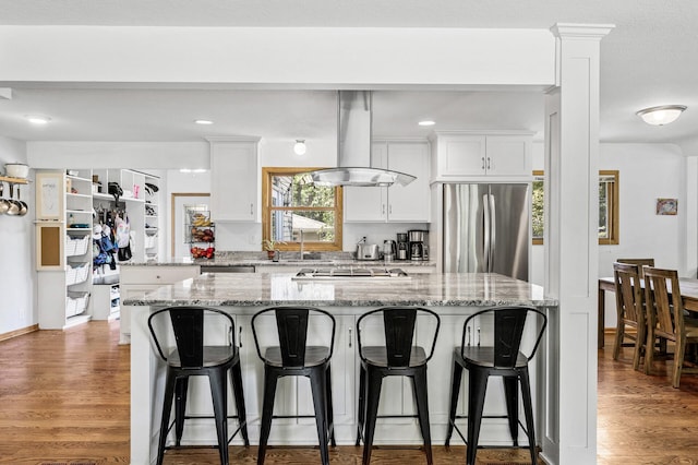 1281 Minnehaha Pkwy, Minneapolis, MN 55419 - kitchen featuring stainless steel appliances, island range hood, white cabinetry, a kitchen breakfast bar, and wood finished floors