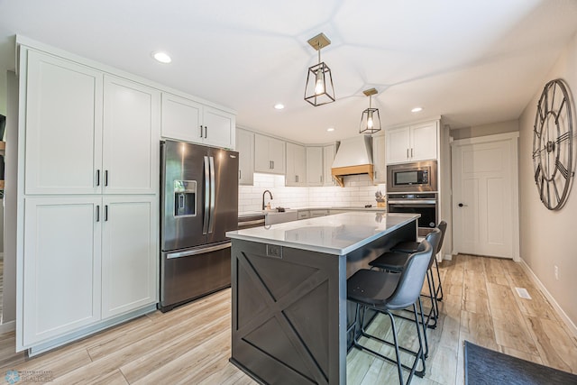 407 6th St NE, Barnesville, MN 56514 - kitchen with appliances with stainless steel finishes, custom range hood, white cabinetry, a kitchen island, and light wood-type flooring