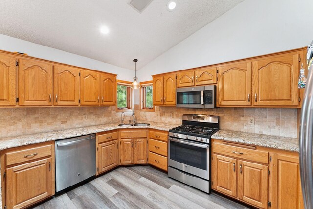 9055 Regent Pkwy, Brooklyn Park, MN 55443 - kitchen featuring appliances with stainless steel finishes, light wood-style floors, brown cabinetry, light stone countertops, and high vaulted ceiling