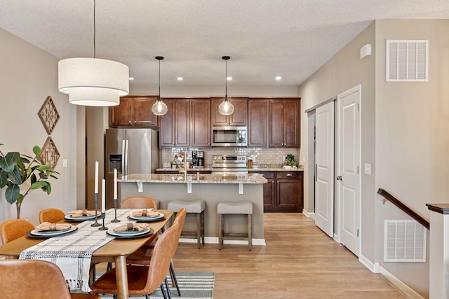 5053 Sunstream Ln, Woodbury, MN 55129 - kitchen featuring appliances with stainless steel finishes, light wood-type flooring, decorative backsplash, an island with sink, and recessed lighting