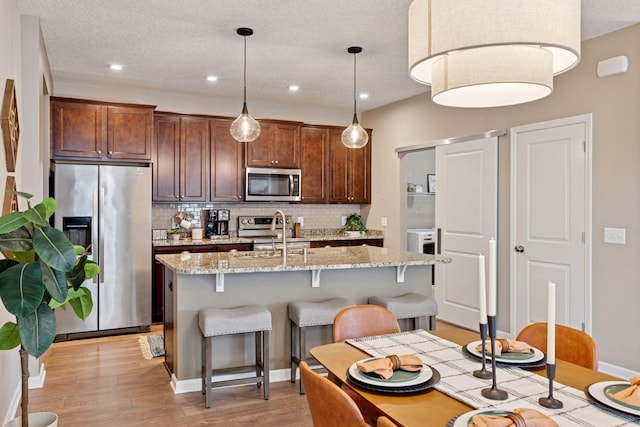 5053 Sunstream Ln, Woodbury, MN 55129 - kitchen with stainless steel appliances, backsplash, light wood-style floors, a center island with sink, and a kitchen bar