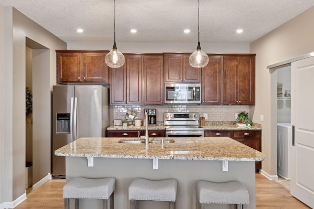 5053 Sunstream Ln, Woodbury, MN 55129 - kitchen with stainless steel appliances, a kitchen island with sink, tasteful backsplash, light wood-type flooring, and a textured ceiling
