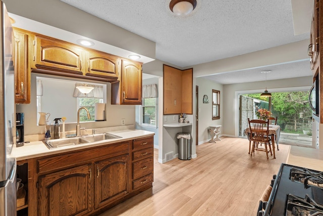 1062 Ohio St, West Saint Paul, MN 55118 - kitchen with light countertops, brown cabinetry, light wood-type flooring, black gas stove, and a textured ceiling