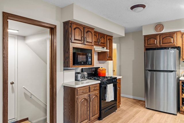 1062 Ohio St, West Saint Paul, MN 55118 - kitchen featuring black appliances, light countertops, under cabinet range hood, light wood-style flooring, and decorative backsplash