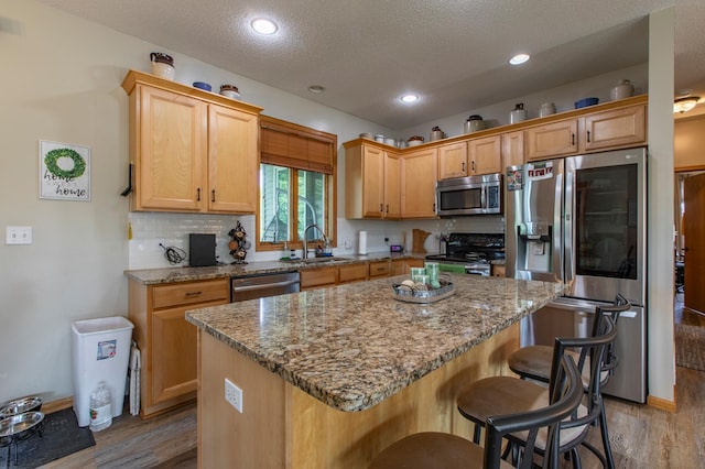 406 13th Ave NW, Kasson, MN 55944 - kitchen featuring stainless steel appliances, light wood-style floors, a breakfast bar area, a kitchen island, and light stone countertops