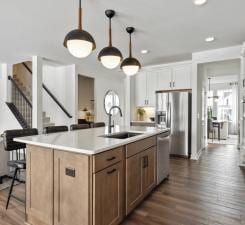 14560 106th Pl N, Maple Grove, MN 55369 - kitchen with dark wood-style flooring, a breakfast bar area, light countertops, a kitchen island with sink, and pendant lighting