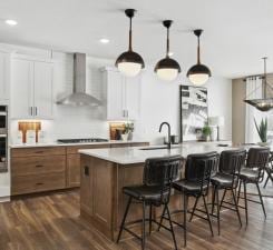 14560 106th Pl N, Maple Grove, MN 55369 - kitchen with wall chimney exhaust hood, black electric stovetop, light countertops, dark wood finished floors, and a center island with sink