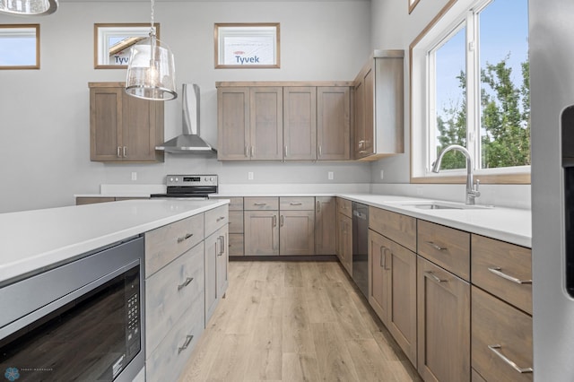 1057 61st Ave W, West Fargo, ND 58078 - kitchen featuring wall chimney range hood, appliances with stainless steel finishes, light wood finished floors, light countertops, and decorative light fixtures
