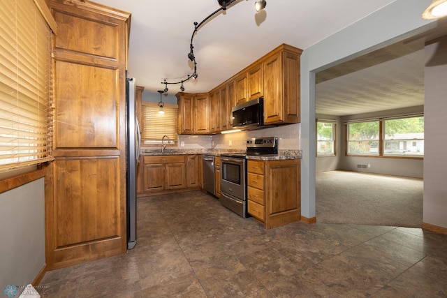 2510 10th St N, Fargo, ND 58102 - kitchen featuring appliances with stainless steel finishes, brown cabinets, tasteful backsplash, dark carpet, and dark stone counters