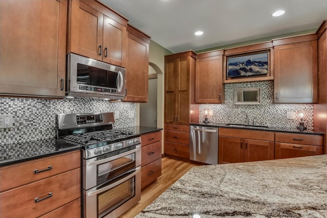 860 Prairie Meadows Dr, Hudson, WI 54016 - kitchen featuring appliances with stainless steel finishes, dark stone counters, light wood-style flooring, arched walkways, and tasteful backsplash