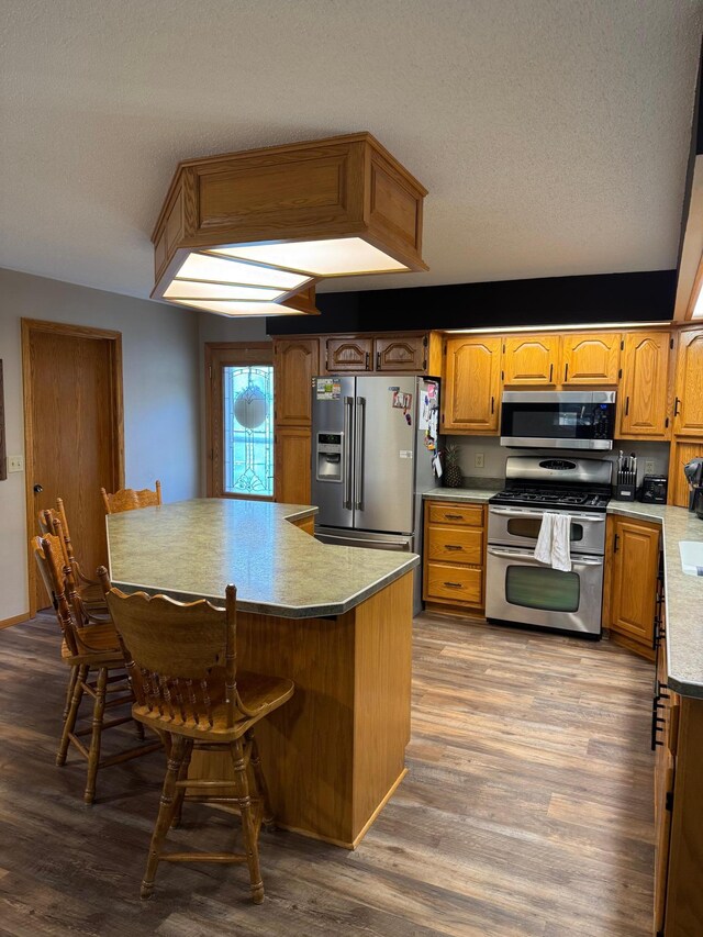121 Park St, Luverne, MN 56156 - kitchen featuring stainless steel appliances, wood finished floors, a textured ceiling, a breakfast bar, and brown cabinets