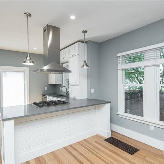 20 12th St NE, Rochester, MN 55906 - kitchen with island exhaust hood, stainless steel gas stovetop, light wood-style floors, white cabinets, and a peninsula