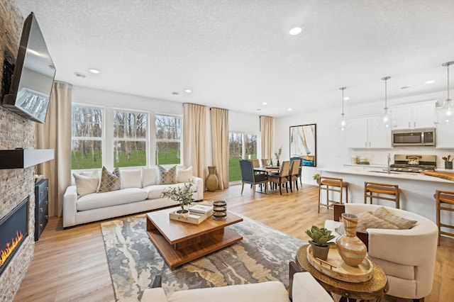 6501 Tamarack Ln, Corcoran, MN 55340 - living area with a stone fireplace, healthy amount of natural light, light wood-style floors, a textured ceiling, and recessed lighting