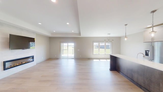 2334 9th St W, Albert Lea, MN 56007 - unfurnished living room featuring light wood-style flooring, recessed lighting, a glass covered fireplace, and a tray ceiling