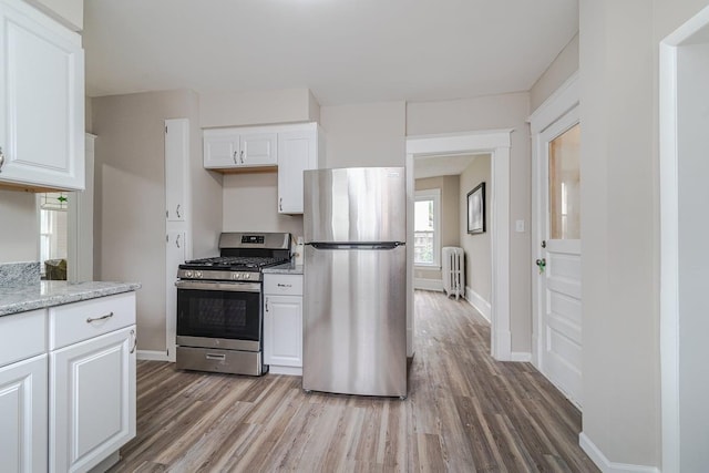 2156 Saint Anthony Ave, Saint Paul, MN 55104 - kitchen featuring stainless steel appliances, radiator heating unit, wood finished floors, white cabinetry, and light stone counters