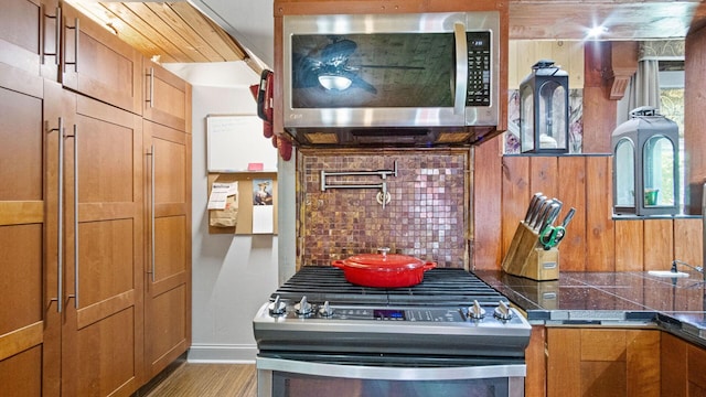 W13263 Hutchinson Rd, Big Bend Twp, WI 54819 - kitchen with stainless steel appliances, backsplash, brown cabinetry, and wood finished floors