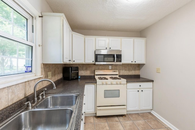 1290 Matilda St, Saint Paul, MN 55117 - kitchen featuring stainless steel microwave, white range with gas stovetop, dark countertops, white cabinets, and tasteful backsplash