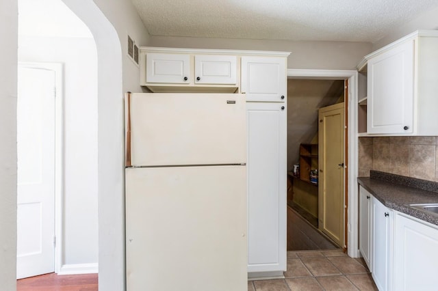 1290 Matilda St, Saint Paul, MN 55117 - kitchen with freestanding refrigerator, dark countertops, white cabinets, backsplash, and a textured ceiling