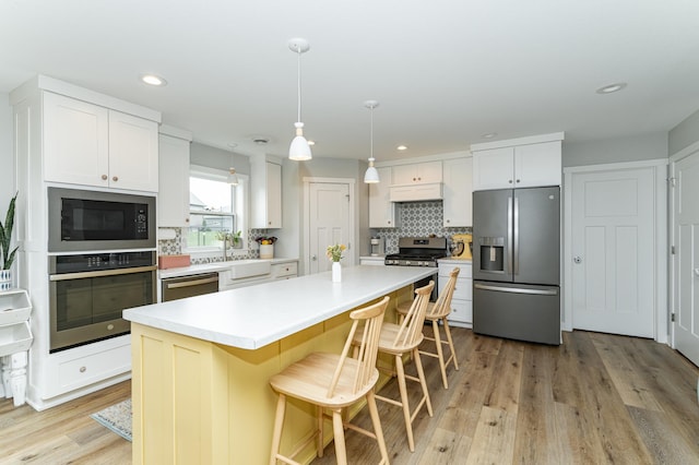 2990 Pinewood Ridge Dr SE, Rochester, MN 55904 - kitchen featuring appliances with stainless steel finishes, decorative backsplash, light wood-style flooring, a kitchen island, and white cabinets