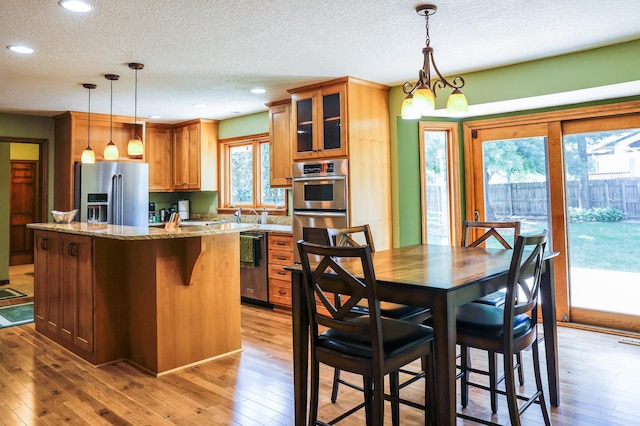 12310 Grouse St NW, Coon Rapids, MN 55448 - kitchen featuring appliances with stainless steel finishes, light wood-style flooring, a center island, a textured ceiling, and brown cabinetry
