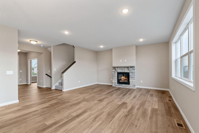 17233 61st St NE, Otsego, MN 55374 - unfurnished living room featuring light wood-style flooring, healthy amount of natural light, stairs, a stone fireplace, and recessed lighting