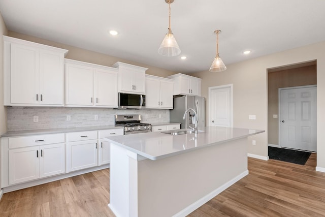 17233 61st St NE, Otsego, MN 55374 - kitchen with stainless steel appliances, light wood finished floors, a center island with sink, backsplash, and white cabinets