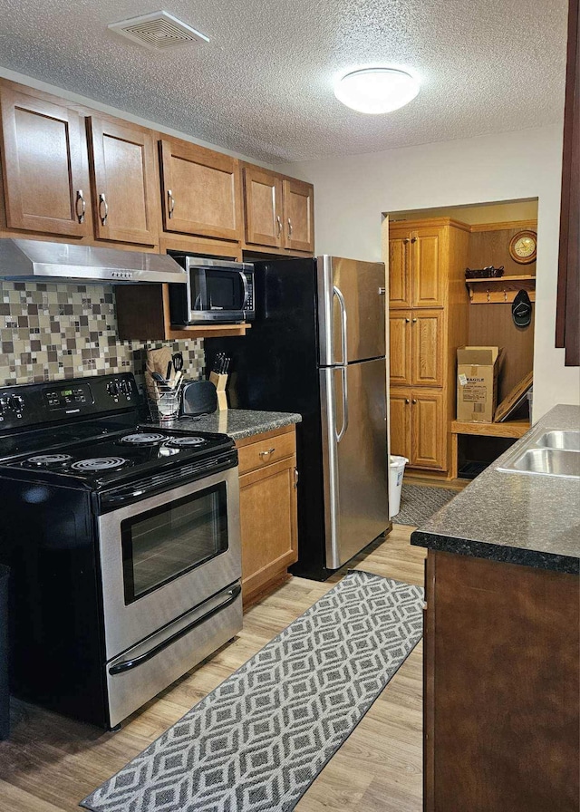 30675 Park St Unit 209, Lindstrom, MN 55045 - kitchen with appliances with stainless steel finishes, exhaust hood, dark countertops, light wood finished floors, and tasteful backsplash