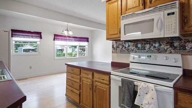 507 15th St SE, Menomonie, WI 54751 - kitchen featuring white appliances, light wood-type flooring, a chandelier, dark countertops, and brown cabinetry