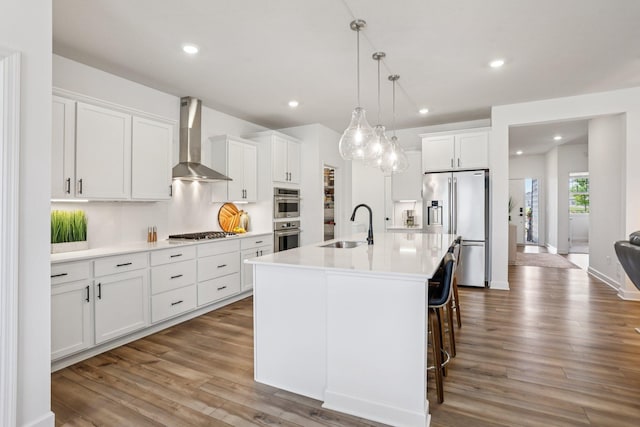 15101 Quince St NW, Andover, MN 55304 - kitchen with appliances with stainless steel finishes, wall chimney exhaust hood, light wood finished floors, a center island with sink, and white cabinetry