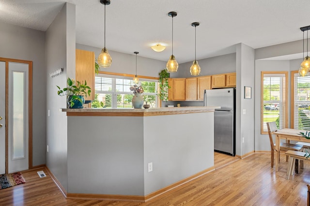1358 Phalen Blvd, Saint Paul, MN 55106 - kitchen with freestanding refrigerator, a peninsula, light wood-style flooring, pendant lighting, and light countertops