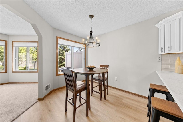 7514 Ojibway Park Rd, Woodbury, MN 55125 - dining room featuring plenty of natural light, a textured ceiling, light wood-style flooring, a chandelier, and arched walkways