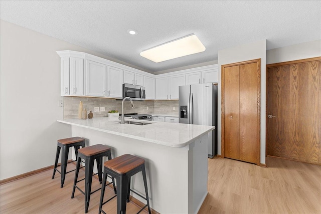 7514 Ojibway Park Rd, Woodbury, MN 55125 - kitchen featuring stainless steel appliances, a peninsula, light wood finished floors, light countertops, and a textured ceiling