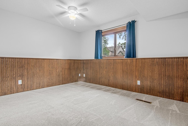 7401 River Shore Ln, Champlin, MN 55316 - spare room featuring wainscoting, carpet flooring, wooden walls, a ceiling fan, and a textured ceiling