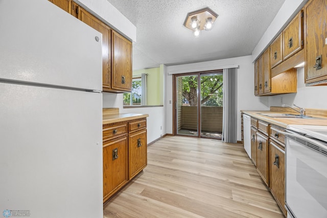 3237 17th Ave S Unit 101, Fargo, ND 58103 - kitchen featuring white appliances, a textured ceiling, brown cabinets, light countertops, and light wood-style flooring