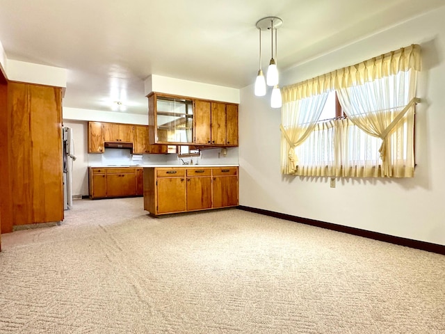 1224 Duba St, Worthington, MN 56187 - kitchen featuring brown cabinets, light carpet, light countertops, pendant lighting, and under cabinet range hood