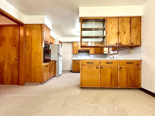 1224 Duba St, Worthington, MN 56187 - kitchen with black oven, brown cabinets, light countertops, under cabinet range hood, and freestanding refrigerator