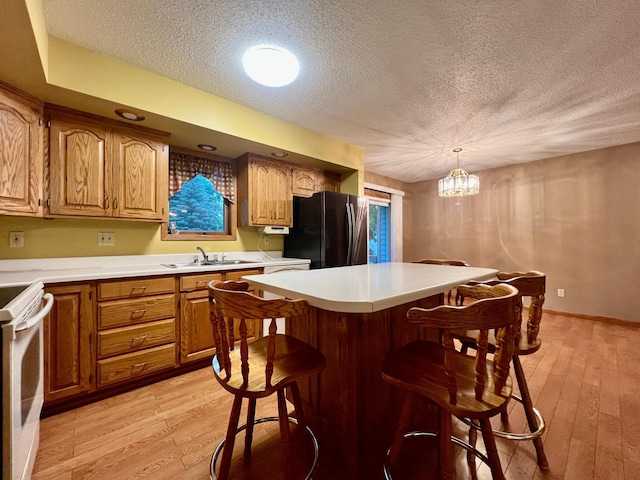1002 6th Ave N, Wheaton, MN 56296 - kitchen with freestanding refrigerator, a textured ceiling, light wood-style flooring, a kitchen bar, and white range with electric stovetop