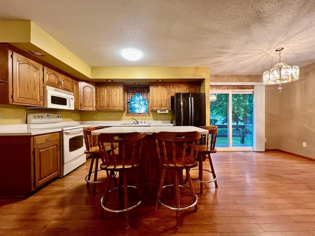 1002 6th Ave N, Wheaton, MN 56296 - kitchen featuring white appliances, hardwood / wood-style flooring, a textured ceiling, light countertops, and a breakfast bar