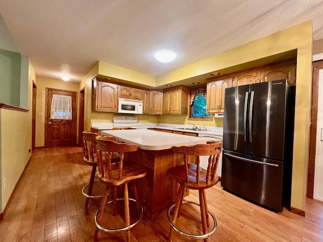 1002 6th Ave N, Wheaton, MN 56296 - kitchen with freestanding refrigerator, white microwave, range, light countertops, and light wood finished floors