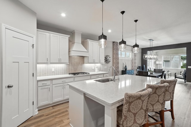 4364 Ginger Dr, Minnetrista, MN 55331 - kitchen with custom range hood, stainless steel gas stovetop, light wood-style flooring, decorative backsplash, and a center island with sink