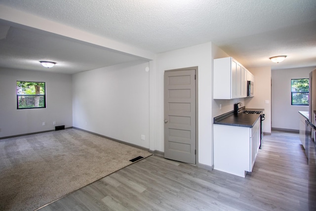422 Park Ave, Sandstone, MN 55072 - kitchen featuring white gas range oven, dark countertops, white cabinets, light wood-style floors, and a textured ceiling