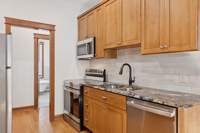 704-706 Holly Ave, Saint Paul, MN 55104 - kitchen featuring appliances with stainless steel finishes, dark stone countertops, tasteful backsplash, light wood-style floors, and brown cabinetry