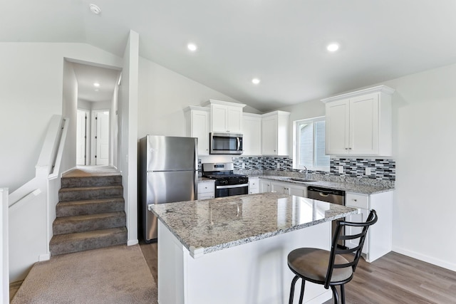 39685 Fallbrook Ave, North Branch, MN 55056 - kitchen featuring appliances with stainless steel finishes, vaulted ceiling, a kitchen island, white cabinets, and light stone countertops
