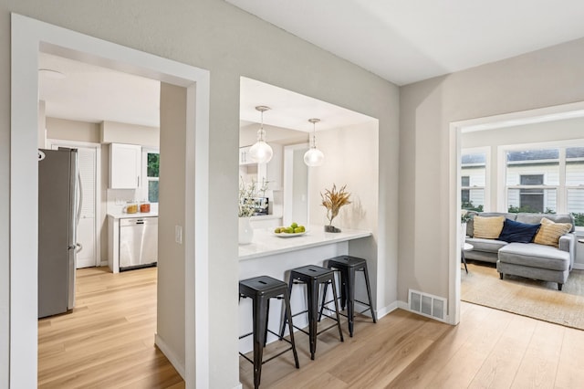 5912 Bartlett Blvd, Mound, MN 55364 - kitchen with stainless steel appliances, light wood-type flooring, white cabinetry, a kitchen bar, and healthy amount of natural light