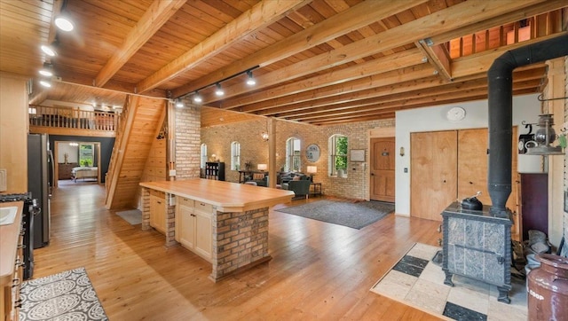 8825 Greeley Loop, Royalton Twp, MN 55006 - kitchen with brick wall, a wood stove, light wood-style floors, track lighting, and a wood ceiling with exposed beams